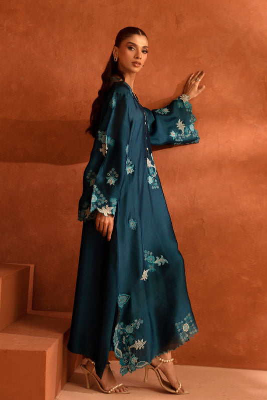 Woman in a teal floral dress standing against an orange wall.