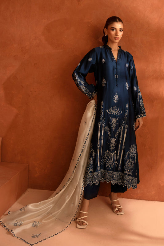 Woman wearing a dark blue embroidered traditional outfit with a beige dupatta against a brown background
