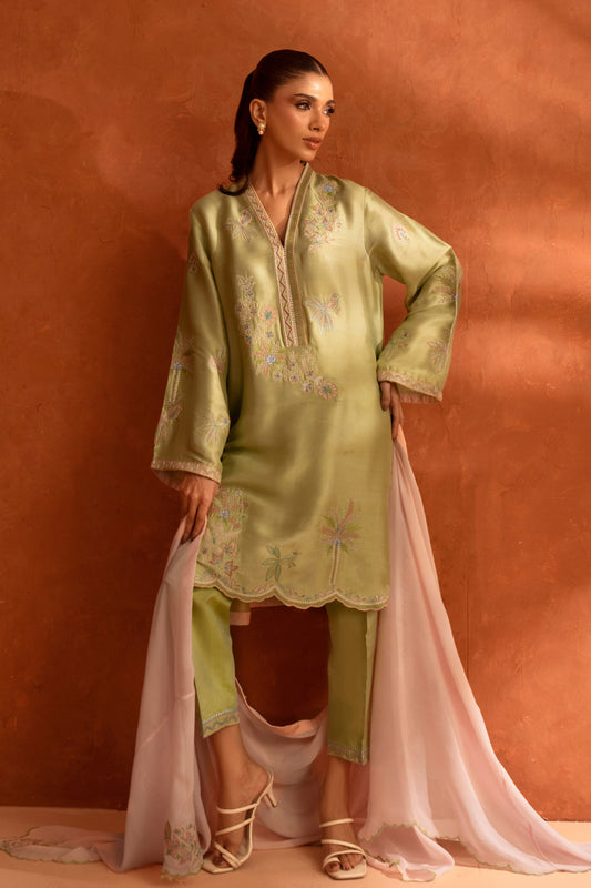 Woman wearing a green embroidered traditional outfit with a plain background