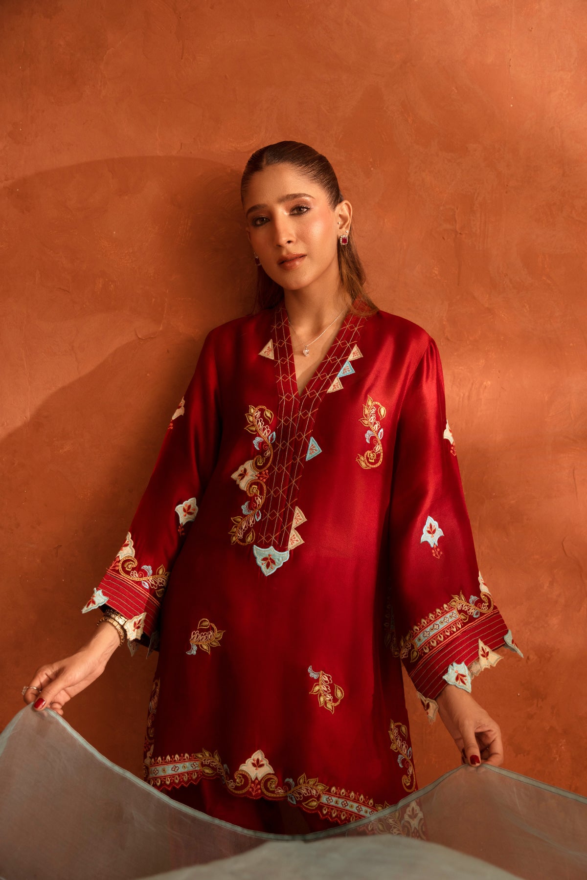 Woman wearing a red embroidered dress against an orange background
