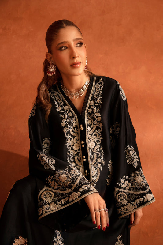 Woman wearing a black embroidered kaftan against an orange background
