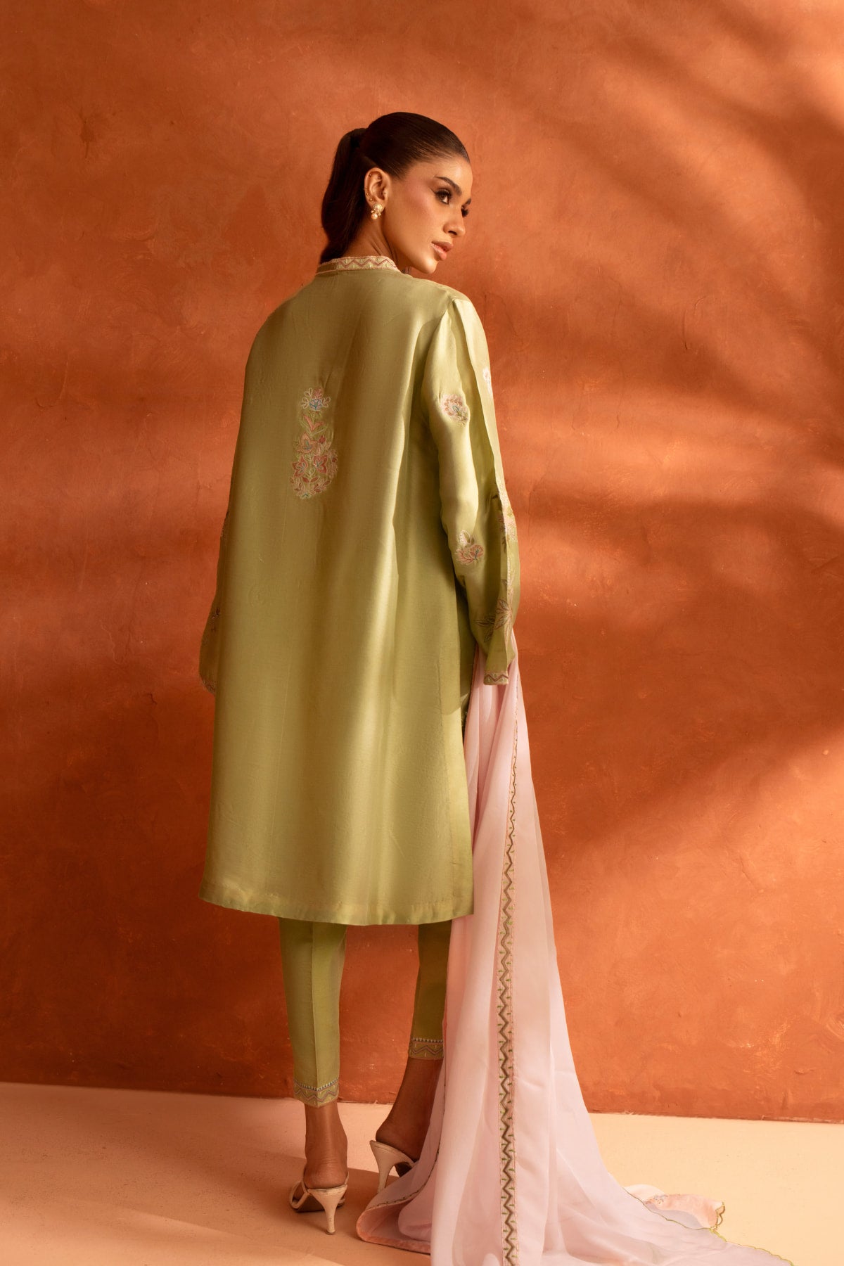 Woman in traditional outfit with green top and pink dupatta against a warm-toned background