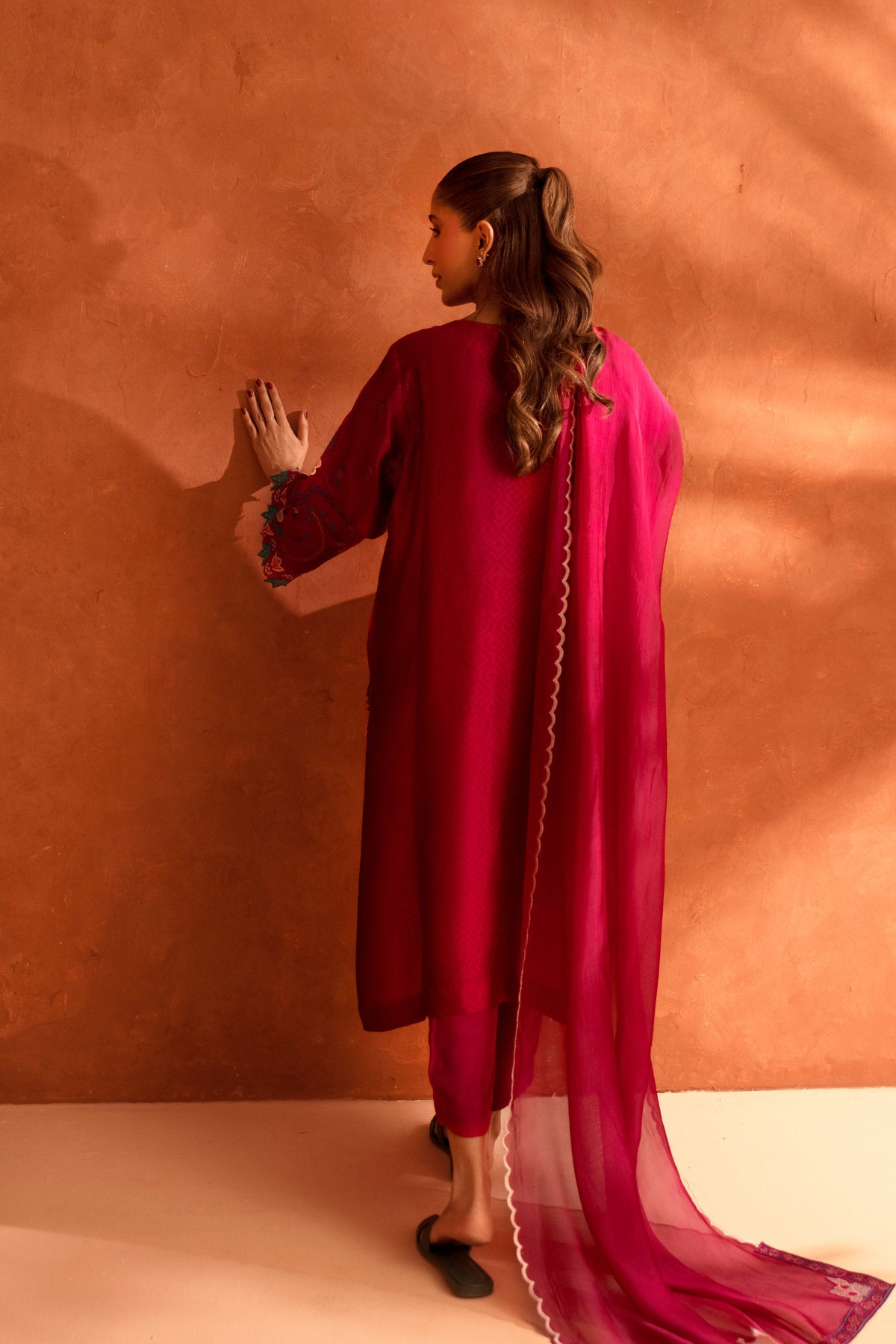 Woman in a red outfit with a pink dupatta against an orange wall