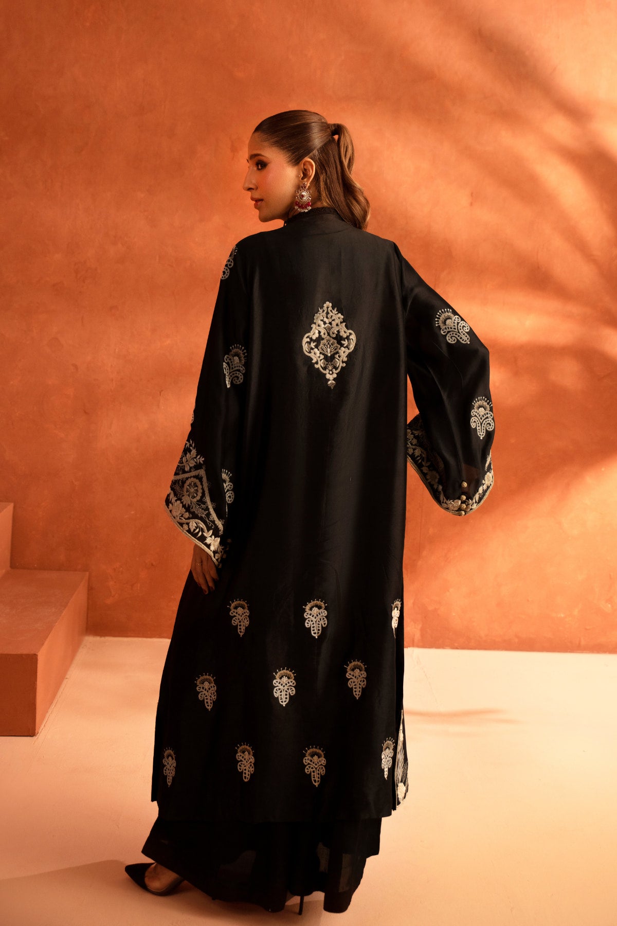 Woman wearing a black dress with white embroidery against an orange background