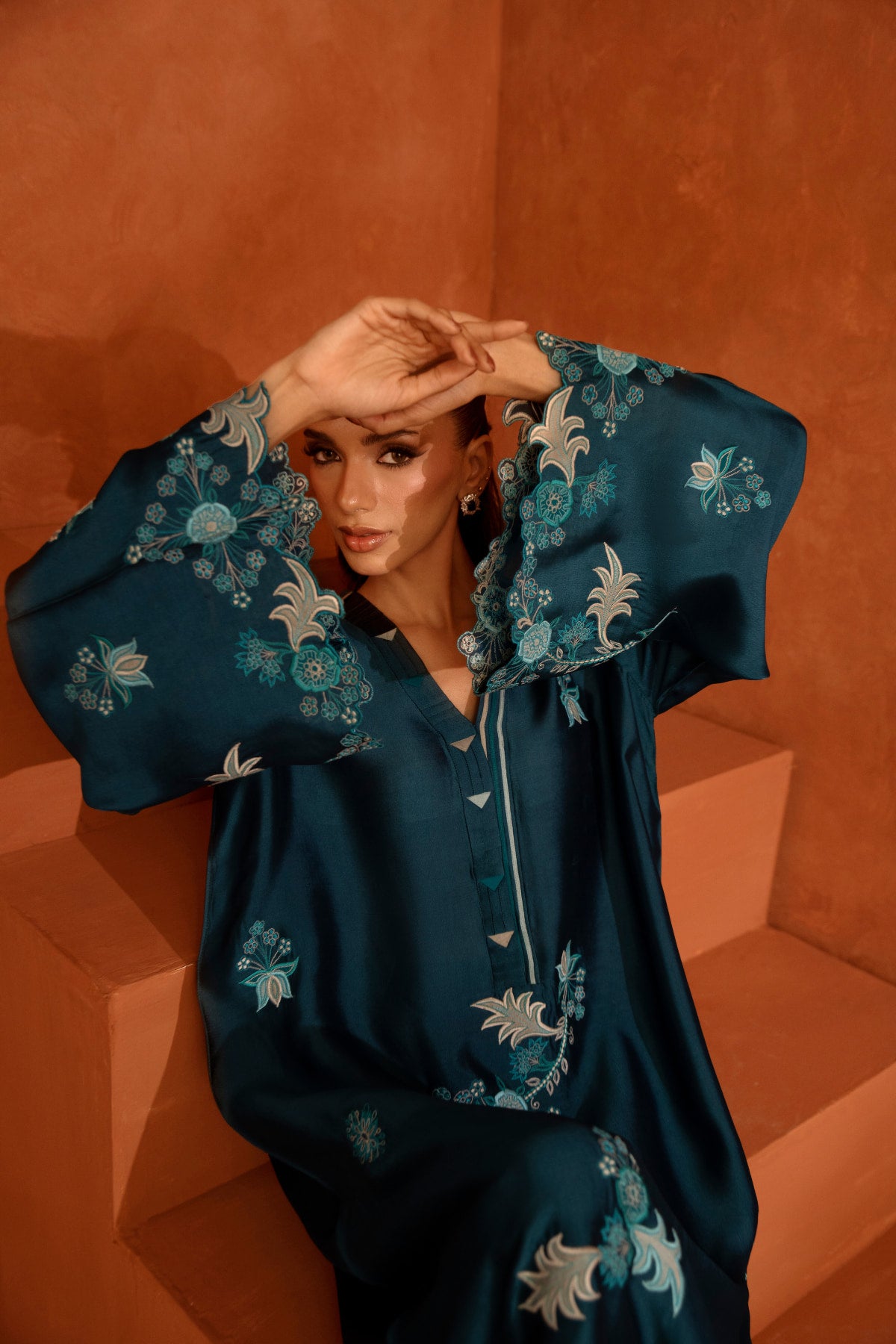 Woman wearing a blue embroidered outfit against an orange background