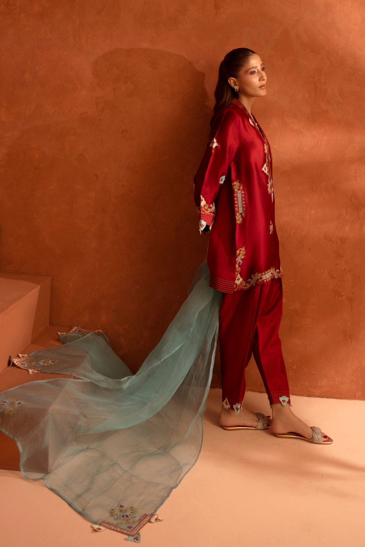 Woman in a red outfit with floral patterns against an orange wall