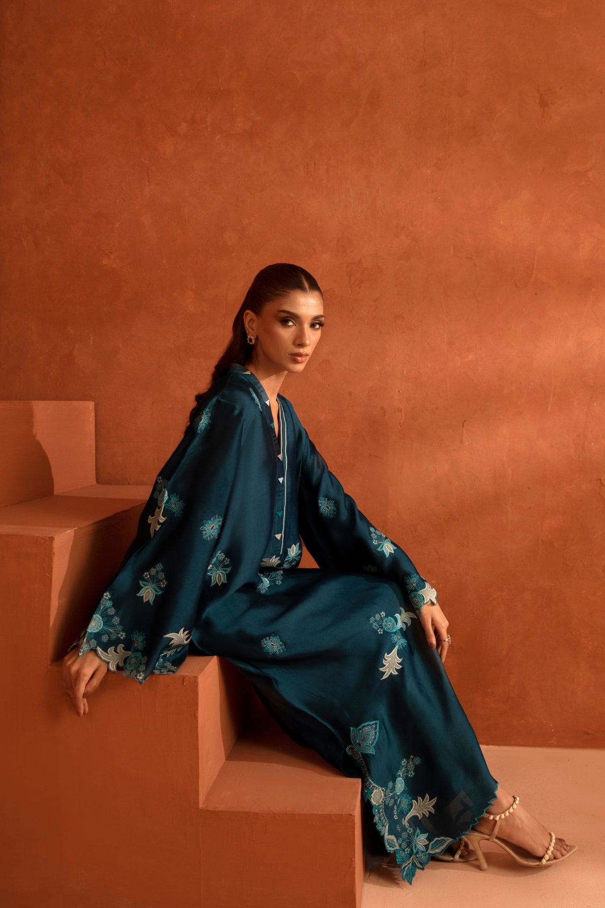 Woman in a dark blue floral outfit sitting on a terracotta step against a matching wall.