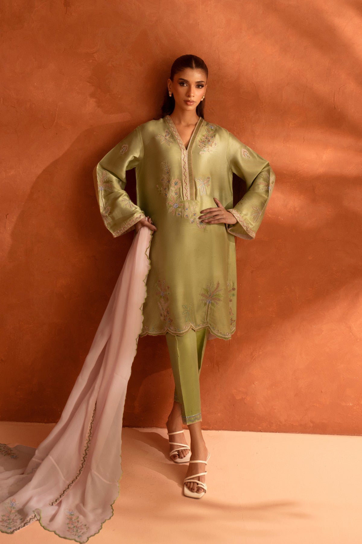Woman wearing a light green traditional outfit with a pink dupatta against an orange background